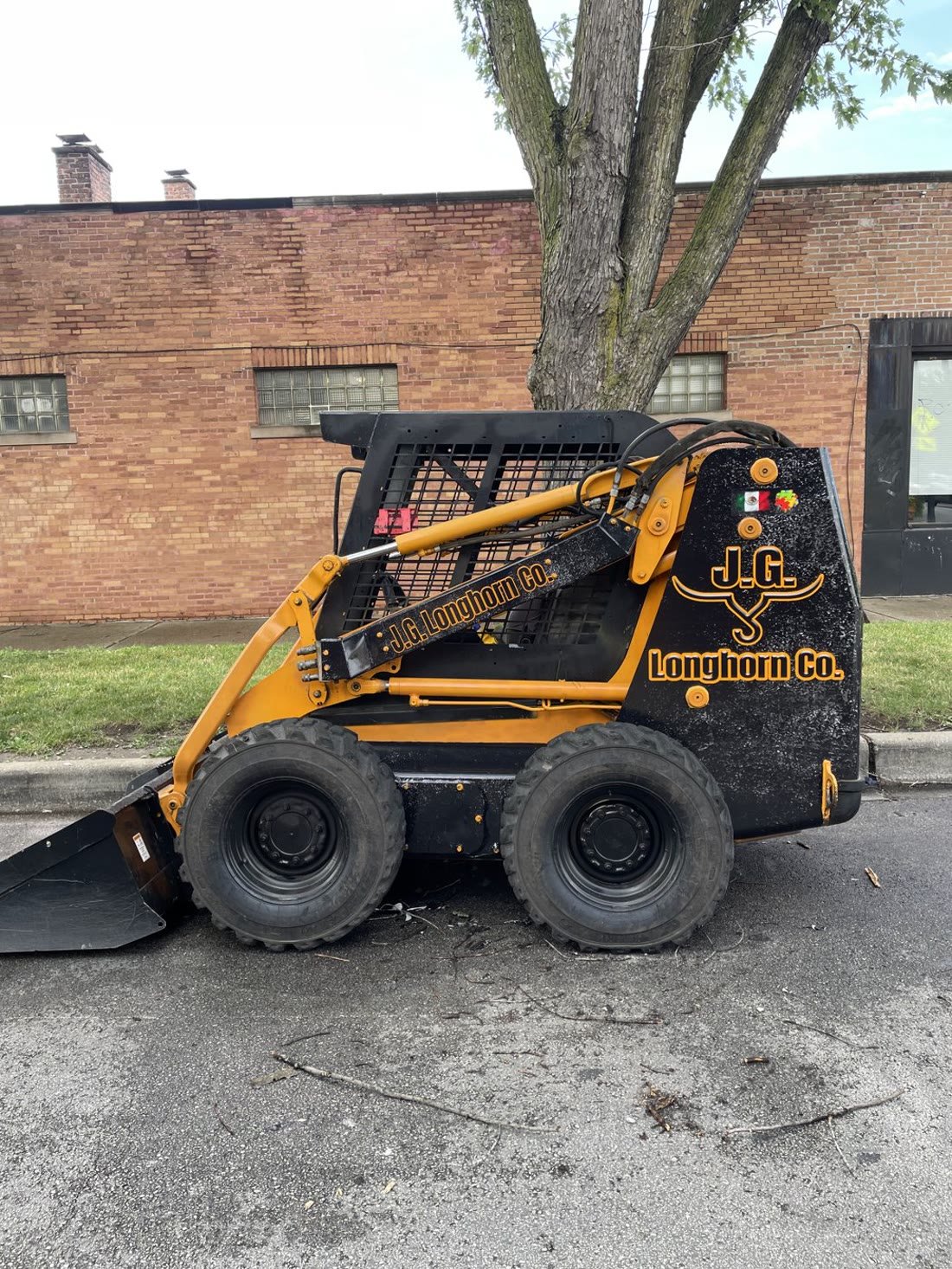 Orange skid steer loader with gold J.G. Longhorn Co. lettering and logo decals