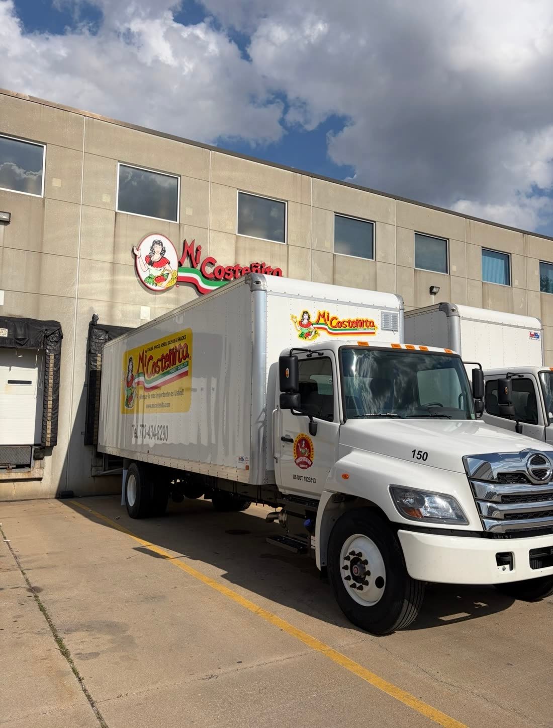 White box truck with a large food company logo decal, parked in front of the warehouse with a matching wall sign