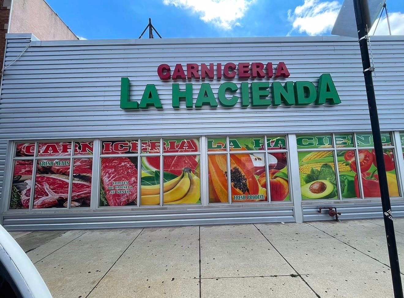 Red and green 3D channel letters reading Carniceria La Hacienda above a storefront with printed meat and produce window graphics
