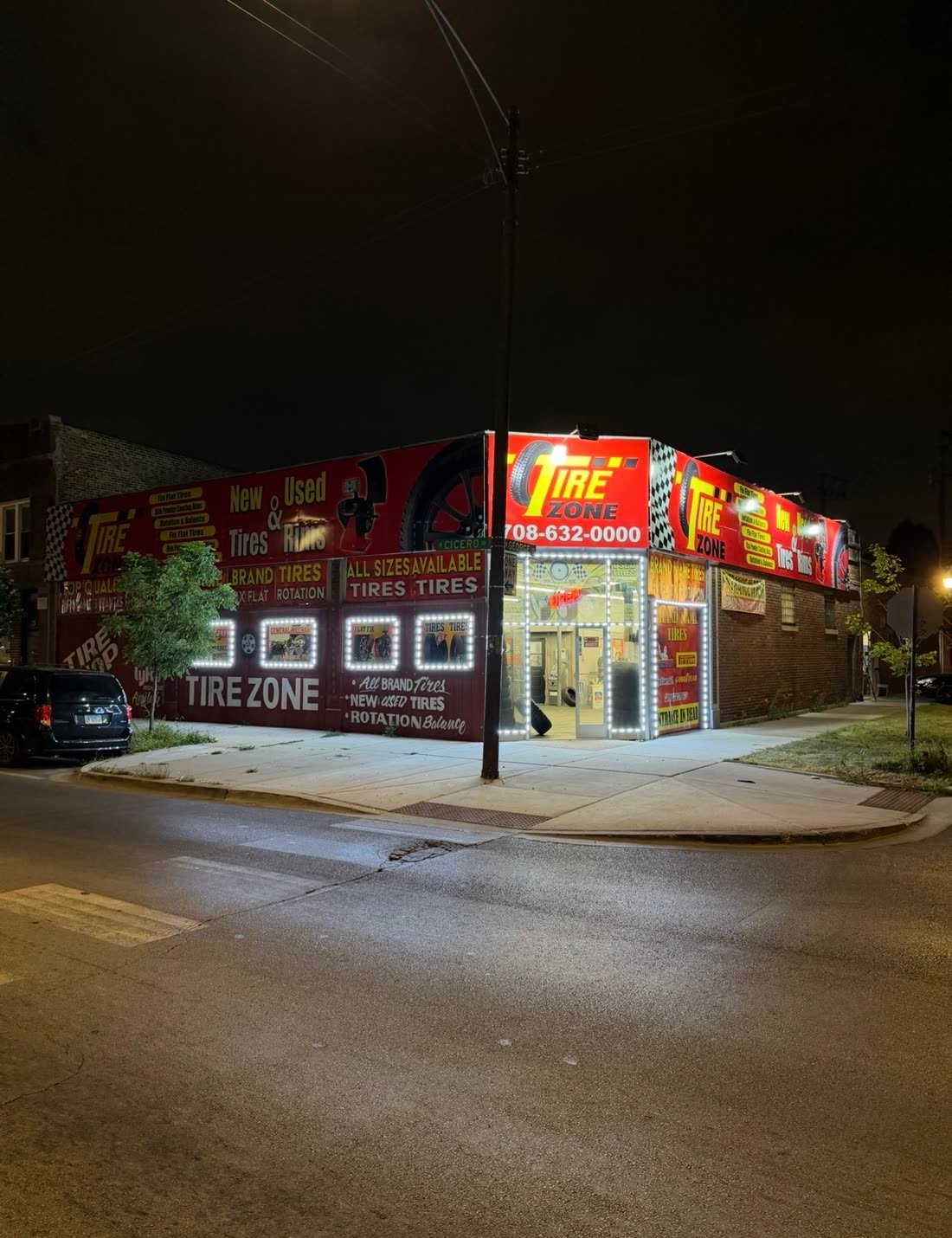 Corner tire shop wrapped in red and yellow signs and banners, lit up at night